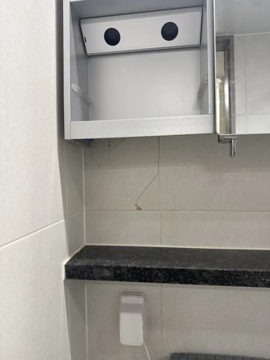 세면대 상부장 아래 벽타일 이음새를 따라 위에서 아래로 가늘게 이어진 헤어라인 크랙이 보이는 작업 전 실제 현장
